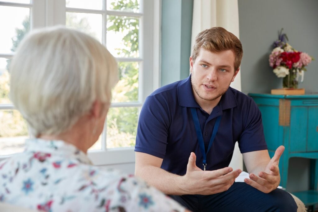 Pflegekraft im Gespräch mit einer älteren Frau in deren Wohnung